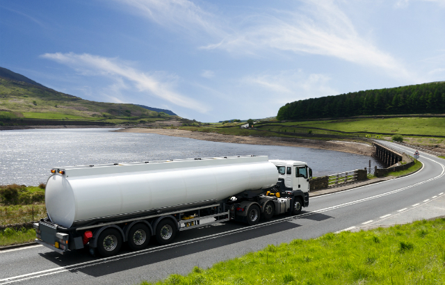 A tanker driving on a winding road near a lake.