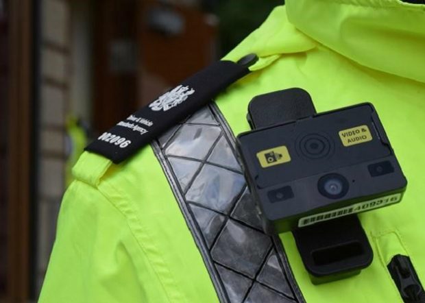 A body camera affixed to the chest of a DVSA officer in a high-vis jacket. The camera bears a sticker saying 'Video & Audio'