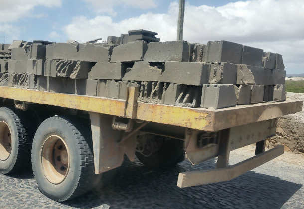 A flat bed vehicle, with no sides. loaded with grey bricks that aren't tied down by any straps or ropes.