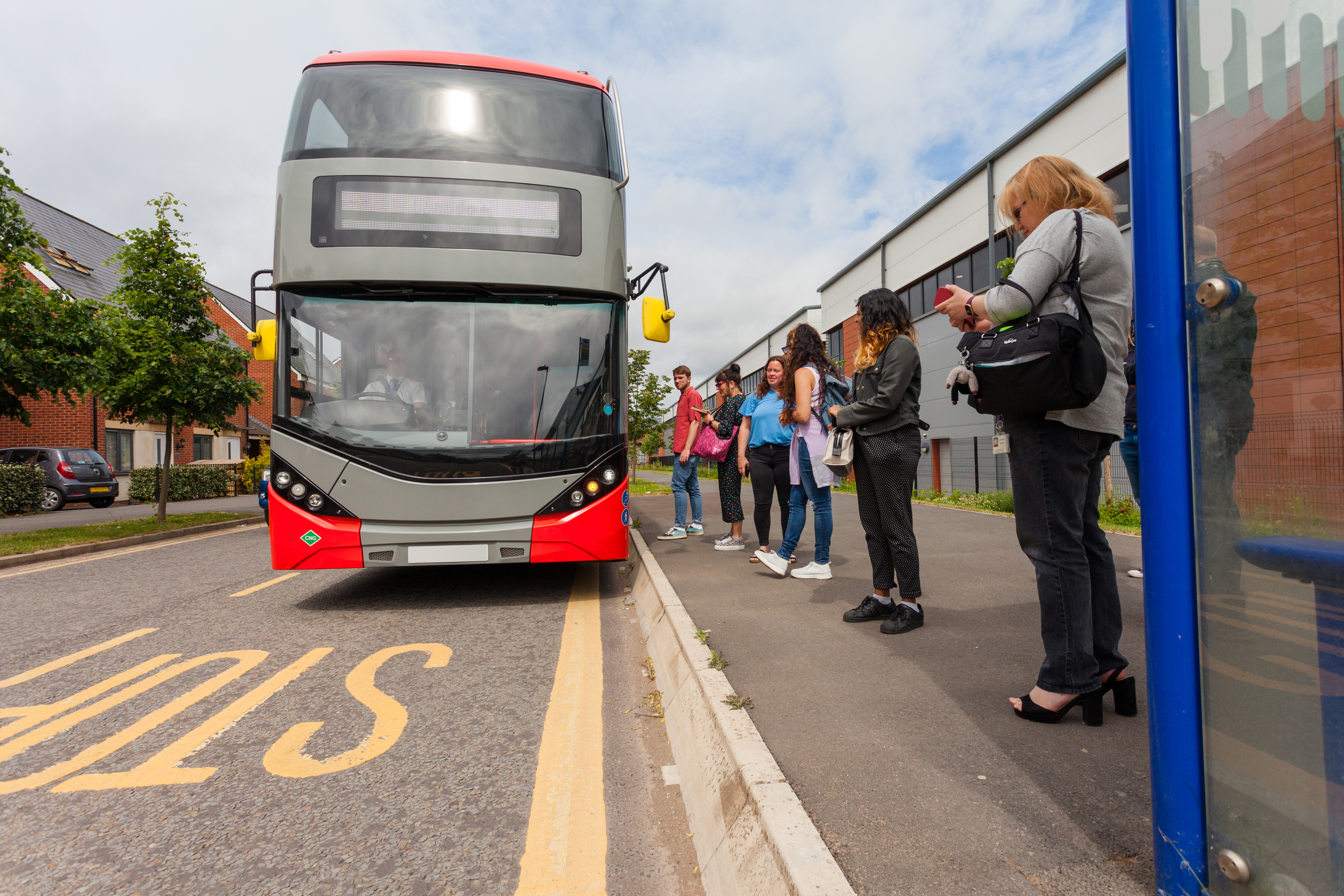 Red and grey bus on street with passengers waiting at stop